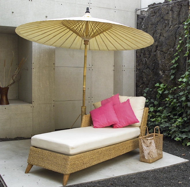 Wicker chaise lounge with umbrella and pillows.